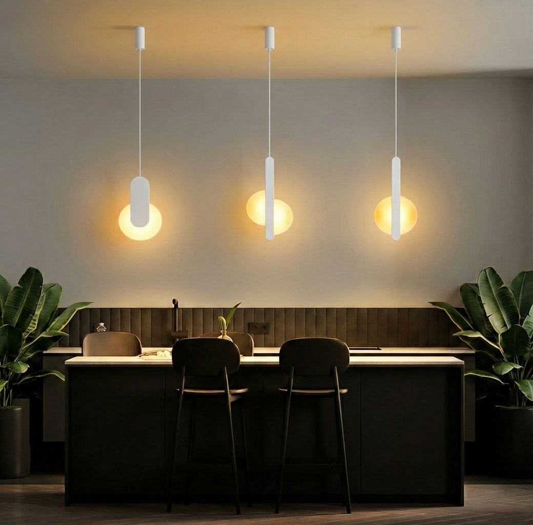  Trio of white Matchstick Slice Pendant Lights over a kitchen bar, their clean silhouettes and warm frosted illumination creating an inviting gathering space, by Domus Collective.