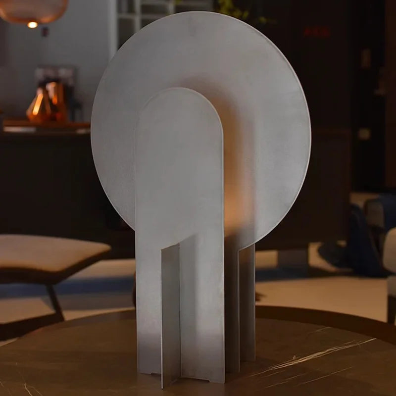 Monumental Eye Table Lamp on a minimalist credenza, polished aluminium disc with signature eye-shaped aperture delivering soft internal glow for curated interiors, by Domus Collective.