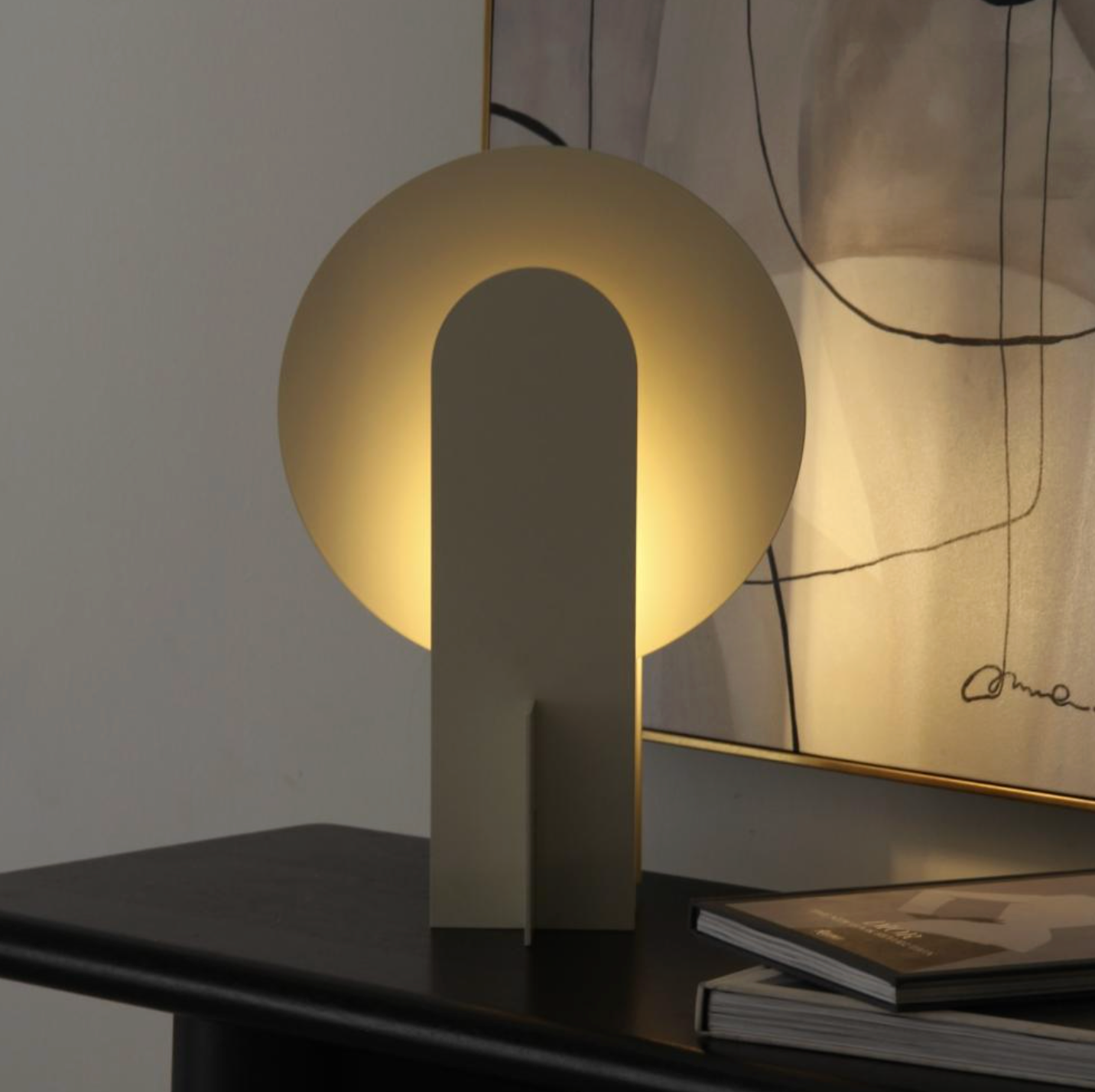 Monumental Eye Table Lamp in brushed gold aluminium, sculptural lighting with circular disc and arched cutout emitting warm ambient glow, by Domus Collective.