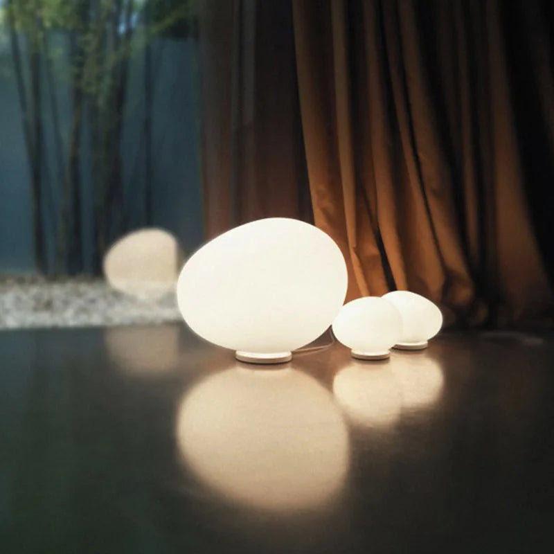 Moonstone Glow Table Lamp collection in multiple sizes arranged on a polished floor at dusk, frosted glass orbs emitting warm diffused illumination for indoor and outdoor spaces, by Domus Collective.