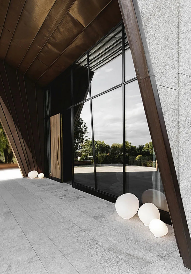 Architectural setting featuring Moonstone Glow Table Lamps in varying sizes, frosted white glass spheres positioned near floor-to-ceiling windows within a modern timber-clad interior, by Domus Collective.