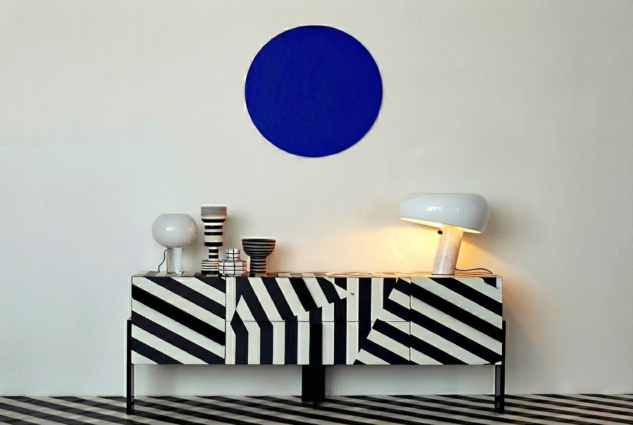 White Mushroom Beam Table Lamp casting warm ambient glow on a bold black and white striped credenza beneath cobalt blue wall art, minimalist contemporary design by Domus Collective.