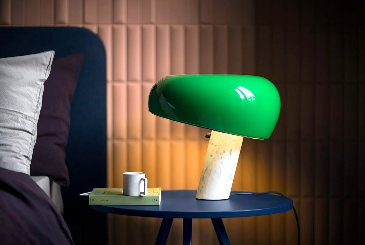 Vibrant orange Mushroom Beam Table Lamp with glowing glass shade on white marble stem atop a green mid-century credenza with graphic art prints, playful retro-inspired lighting by Domus Collective.