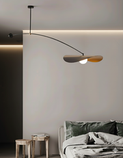 Papilla Pendant Light with sweeping curved arm and butterfly-inspired dual shades in black with warm gold interior, suspended gracefully over a contemporary bedroom setting by Domus Collective.