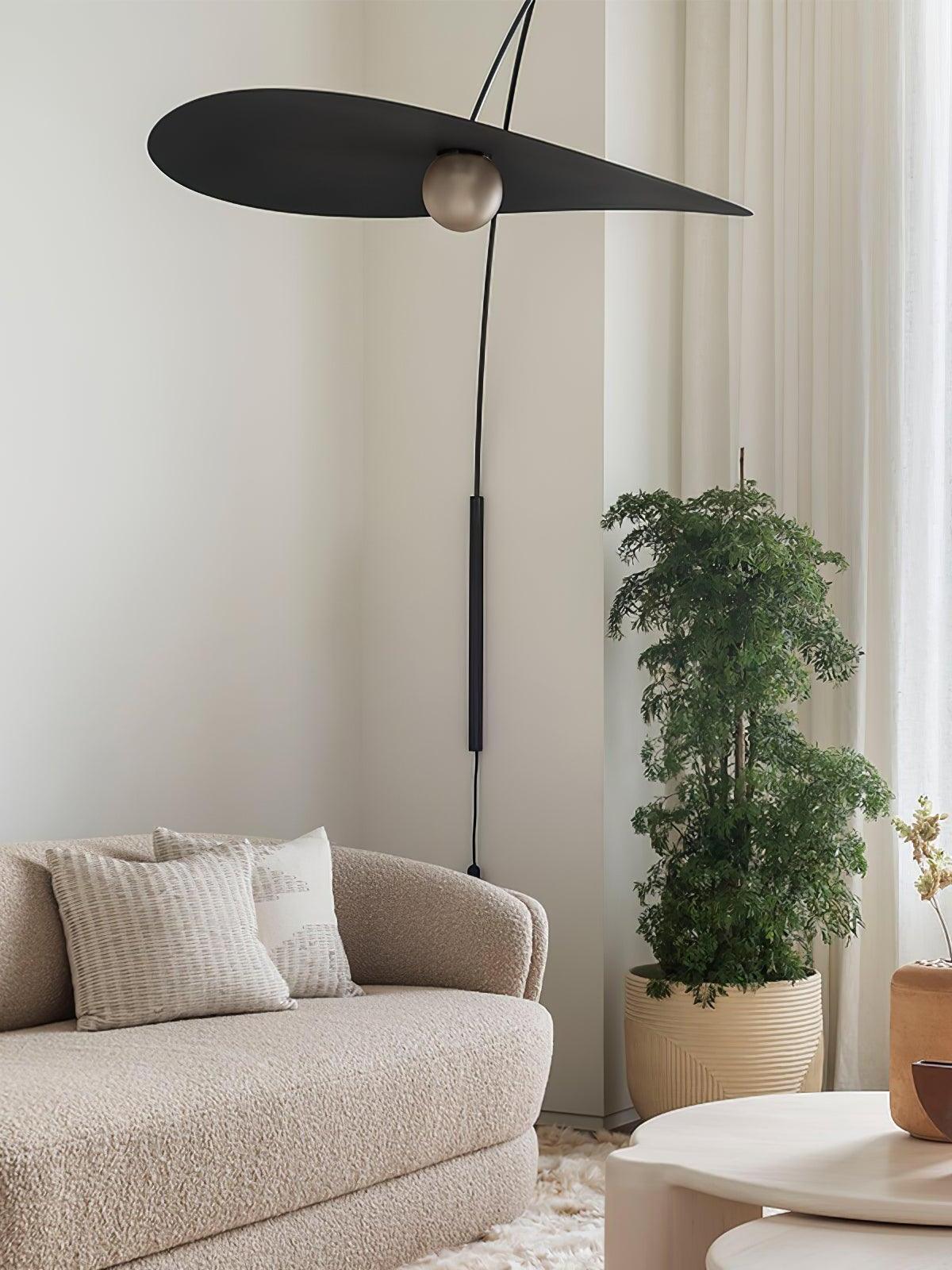 Overhead view of the Papilla Wall Lamp featuring large elliptical matte black shade with decorative metallic sphere, suspended over a textured bouclé sofa in a serene living room setting.