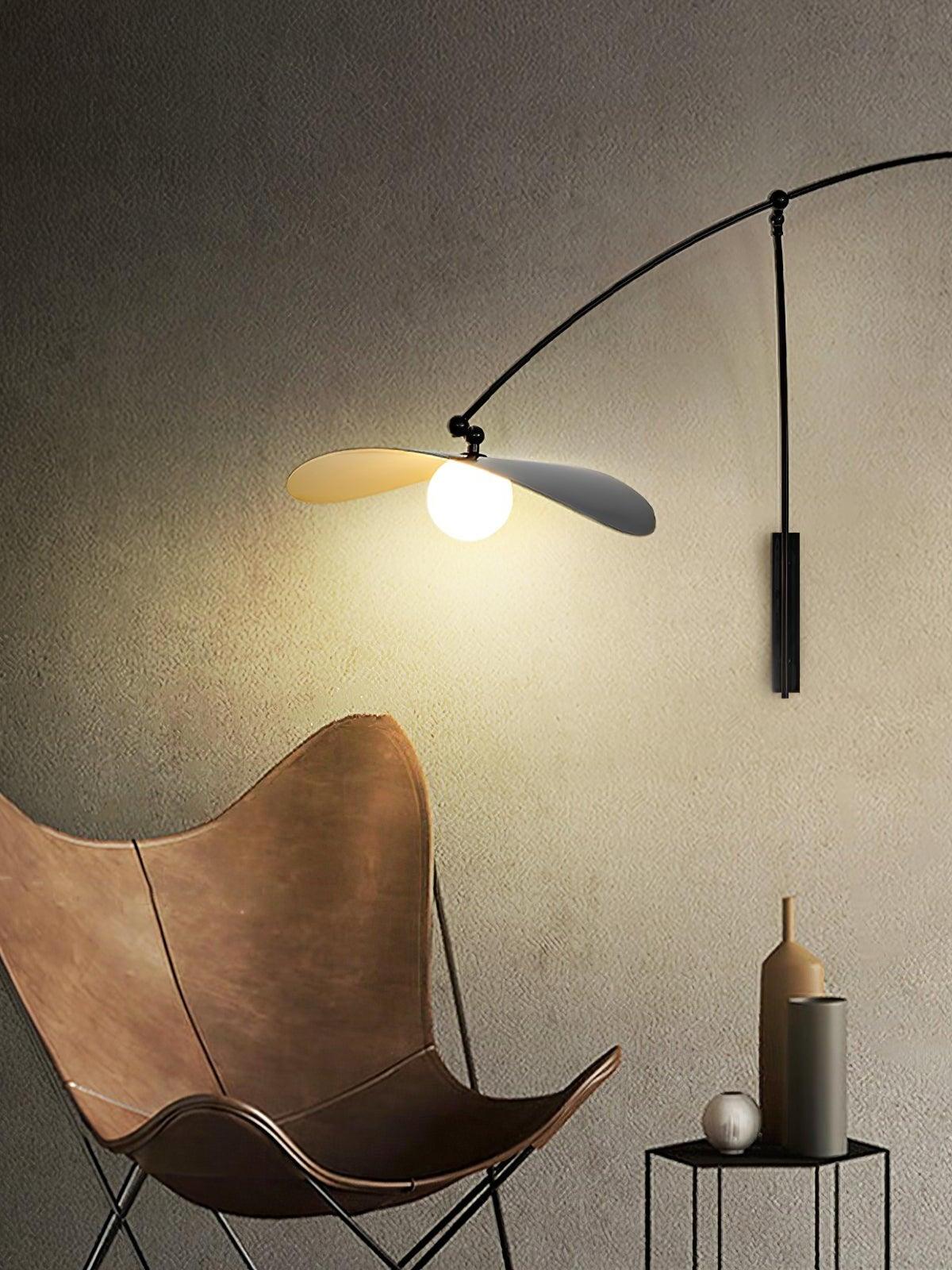 Papilla Wall Lamp illuminating a reading corner, its arched metal arm and overlapping petal shades in blak and golddelivering soft diffused light above a leather butterfly chair by Domus Collective.