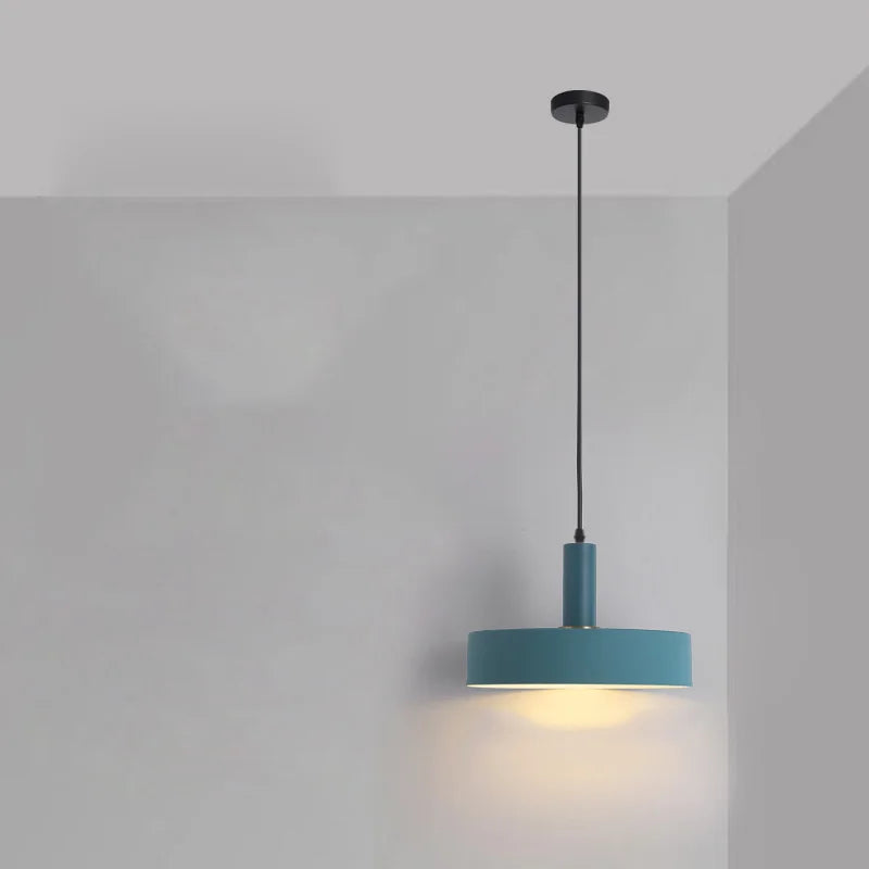 This teal drum shade Pastel Rainbow Pendant Light features a cylindrical stem and brass hardware, bringing retro-modern character to contemporary living areas, by Domus Collective.