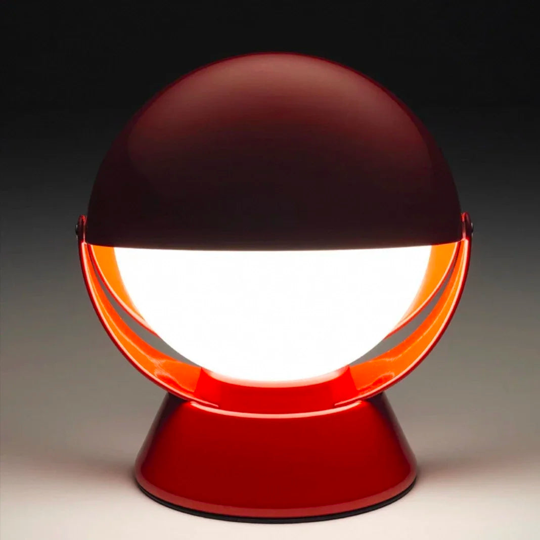 PikaGlow Table Lamp in vibrant red lacquered finish, showcasing its iconic rotating spherical shade cradled in a curved metal frame, emitting soft diffused light for cozy atmospheres.