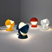 Playful PikaGlow Table Lamps in yellow, navy, red, and white lacquered metal finishes with sculptural spherical shades, casting warm ambient light across a minimalist surface, by Domus Collective.