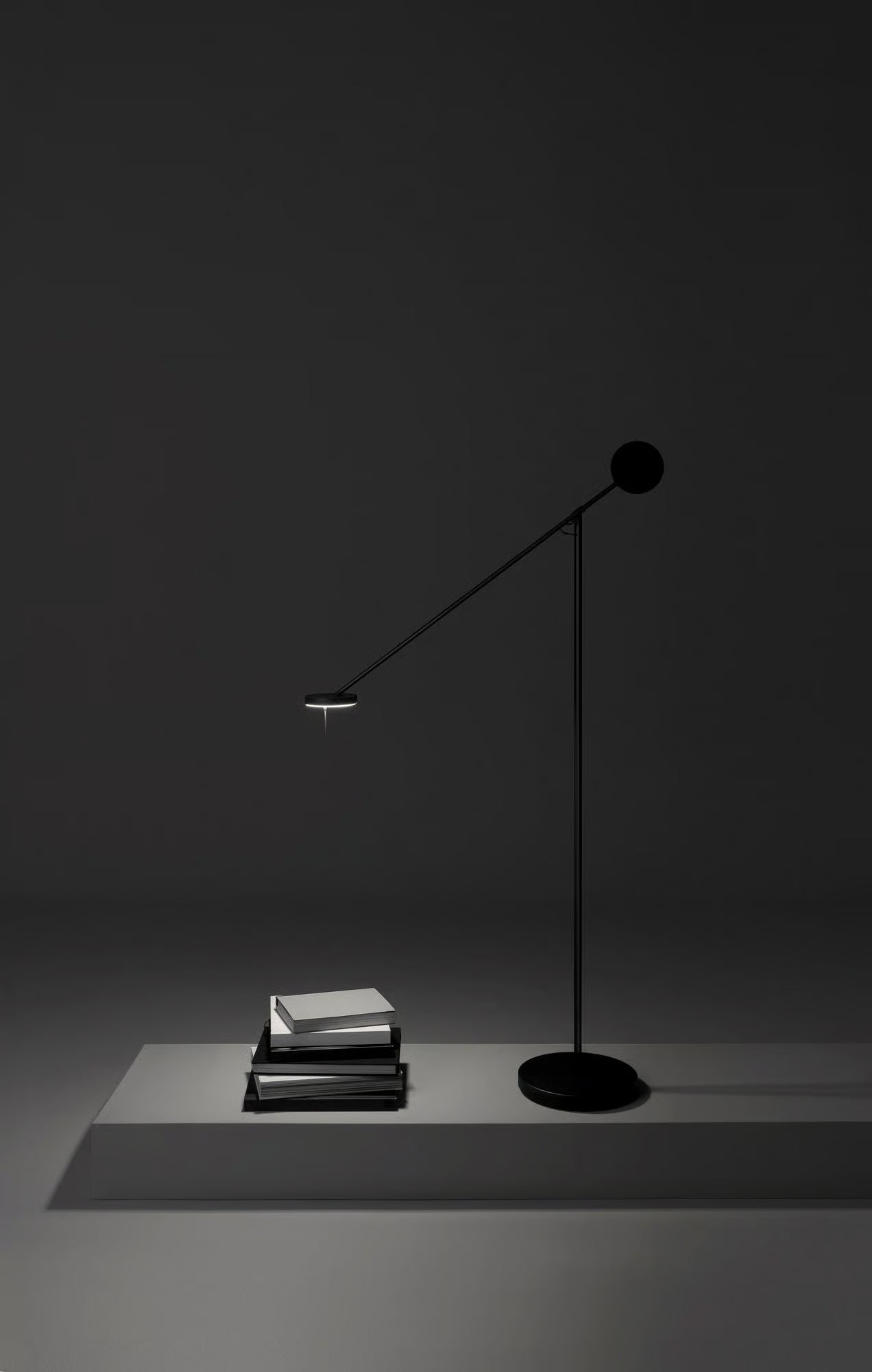 Refined Span Floor Lamp by Domus Collective with diagonal arm and disc counterweight angled over a neutral sofa, its sculptural matte black form silhouetted against a floor-to-ceiling window with garden views.