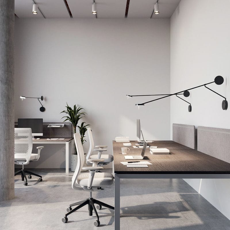 Multiple Refined Span Wall Lights installed in a contemporary open office space, their extended black metal arms and geometric disc elements providing adjustable task lighting for modern workstations.