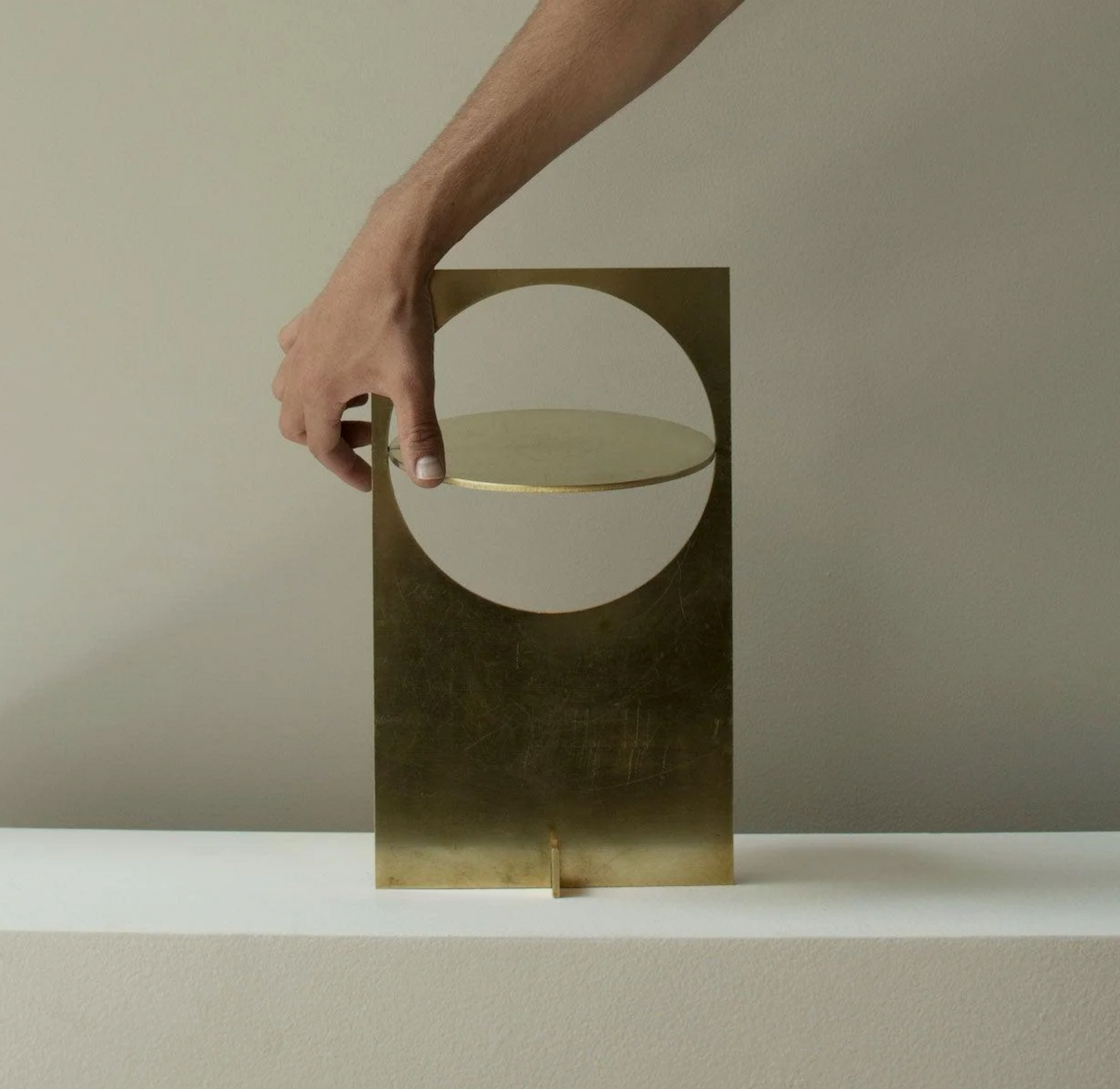 Hand adjusting the turnable reflector disc on Riflesso Table Lamp in aged brass finish, demonstrating the interactive light-directing functionality by Domus Collective.