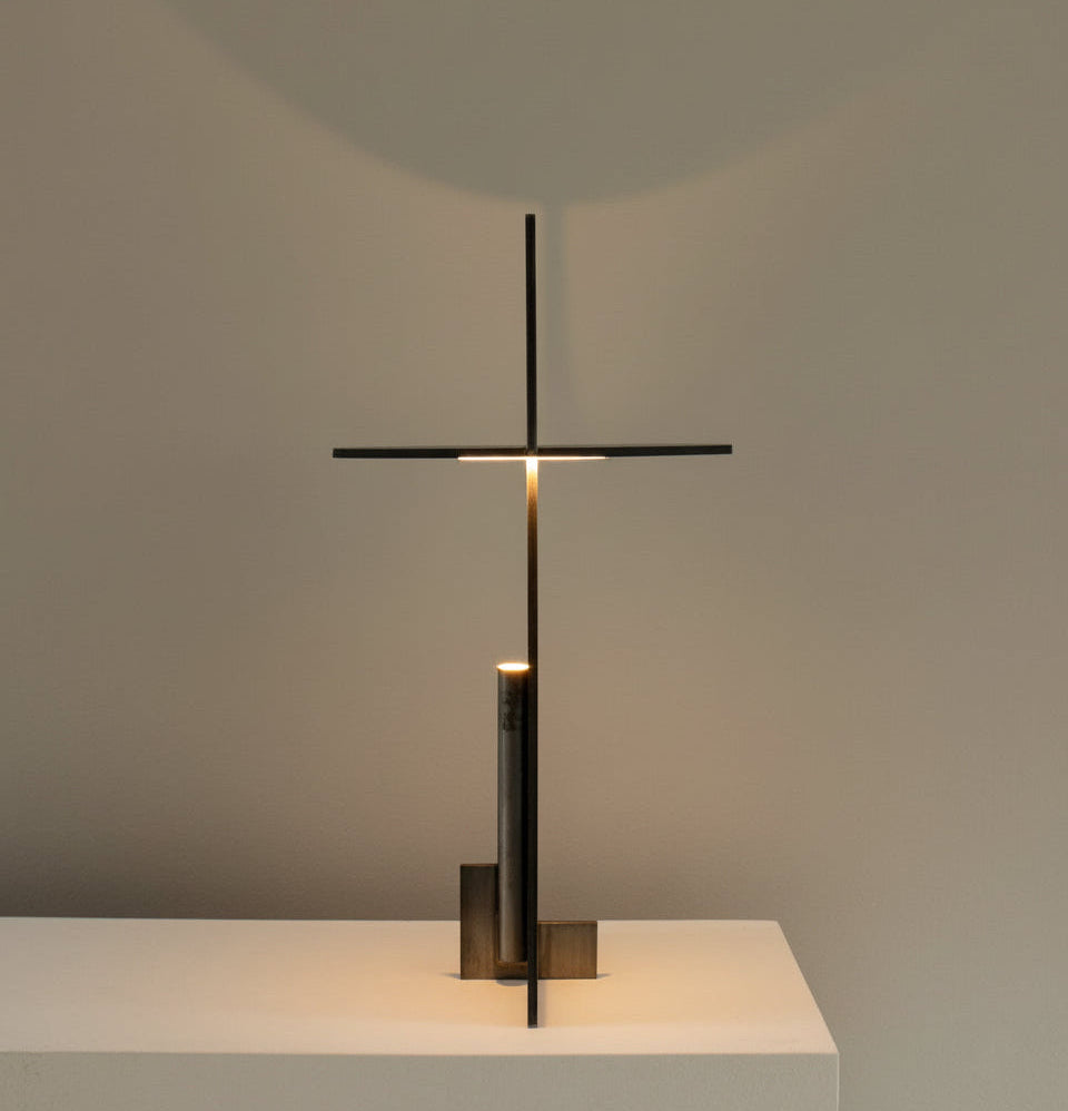 Riflesso Table Lamp alternate design with crossed metal bars and cylindrical light source in bronzed finish, casting sculptural upward glow for artistic interiors by Domus Collective.