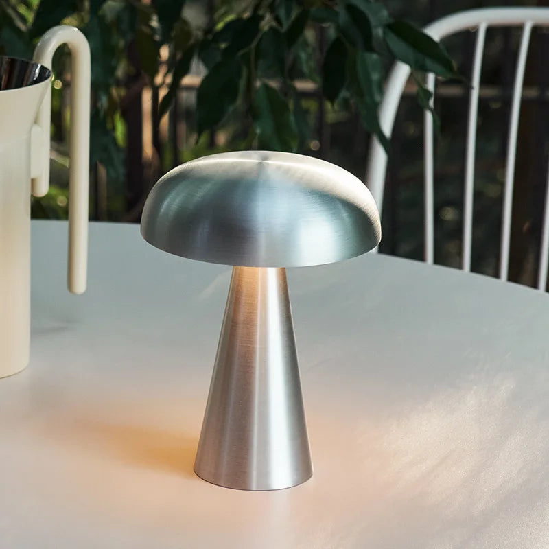 Brushed silver Shroom Aura Portable Lamp on outdoor café table, its sleek metallic finish and organic form adding contemporary elegance to alfresco settings by Domus Collective.