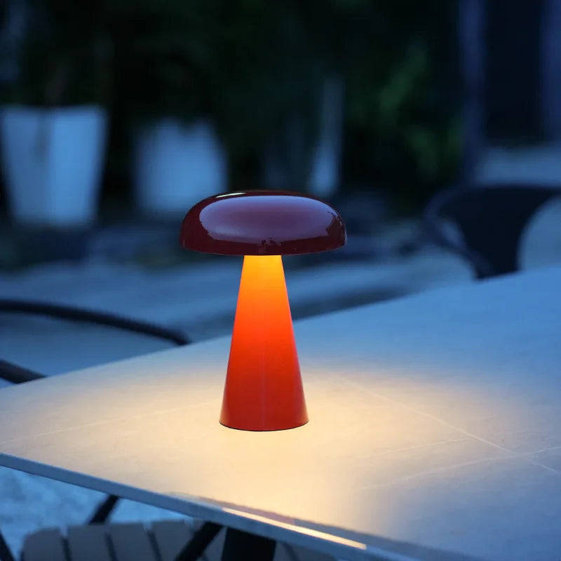 Glossy red Shroom Aura Portable Lamp glowing warmly on evening patio table, demonstrating the portable design and ambient illumination for outdoor entertaining by Domus Collective.