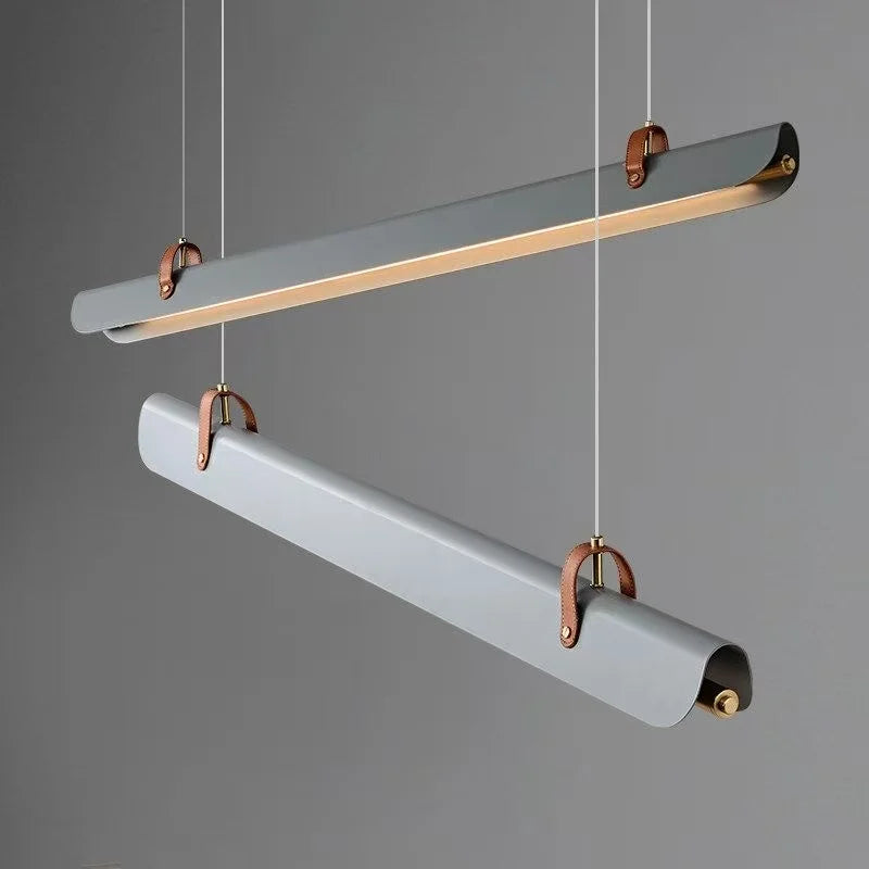 Two modern Sleek Scroll cylindrical pendant lights fixturesby Domus Collective  in a matte gray finish with brass-colored metal brackets and hanging cords, shown against a solid gray background.