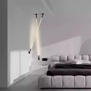 Two Spectra Flex Wall Lights with matte black mounts and warm LED tubes arranged in a dramatic crossed configuration beside a modern upholstered bed, bringing sculptural ambience to minimalist bedrooms, by Domus Collective.