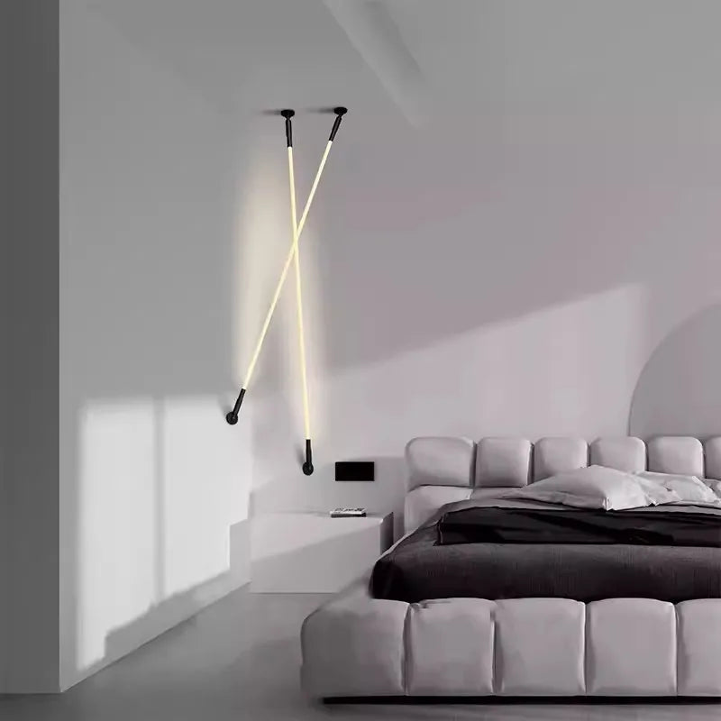 Two Spectra Flex Wall Lights with matte black mounts and warm LED tubes arranged in a dramatic crossed configuration beside a modern upholstered bed, bringing sculptural ambience to minimalist bedrooms, by Domus Collective.