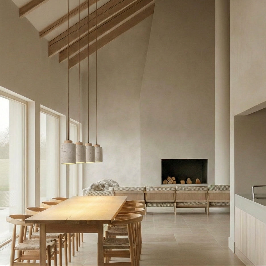 Five oak wood tall, travertine Stone Cylinder Pendant Lamps suspended in a row above a wooden dining table, their organic texture and focused glow complementing exposed beam architecture, by Domus Collective.