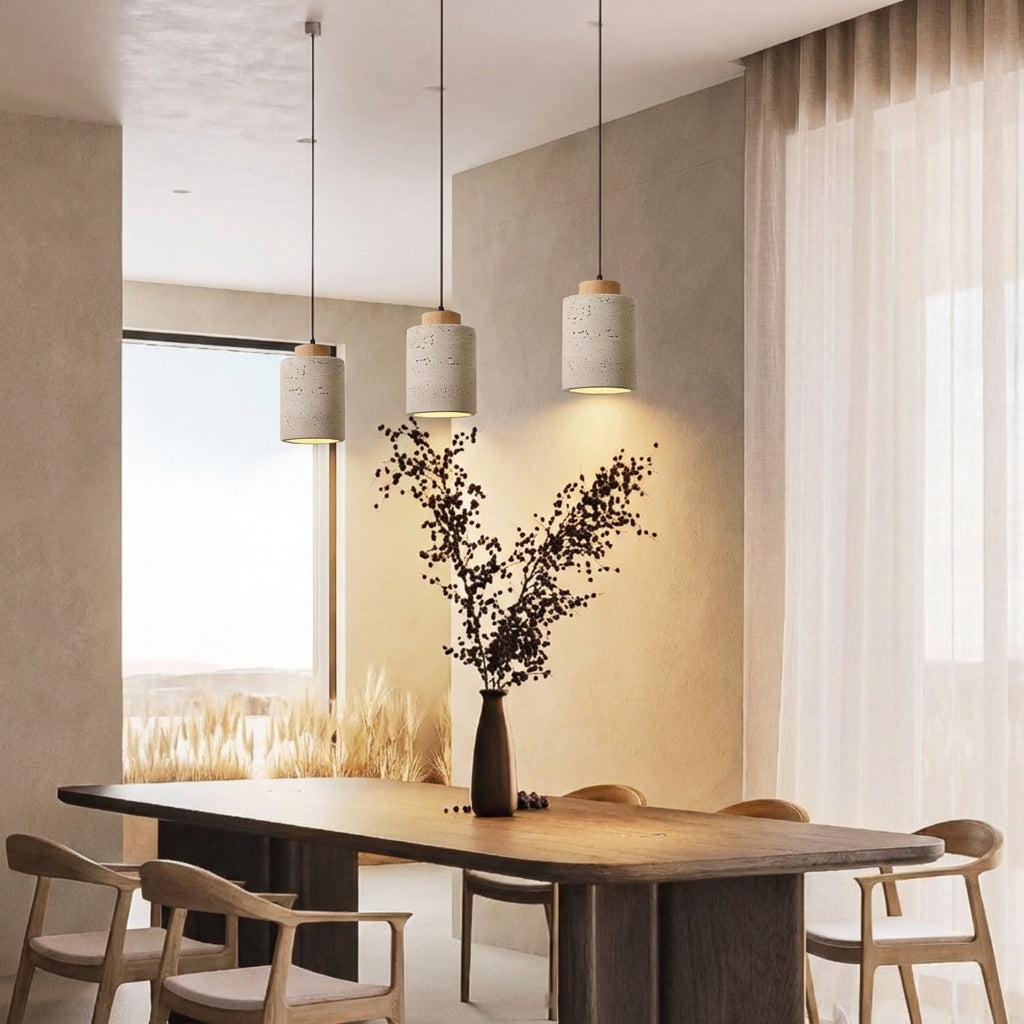 Trio of Three tall Oak Stone Cylinder Pendant Lamps illuminating a minimalist dining space, their natural travertine texture and warm focused light creating an inviting atmosphere for gatherings, by Domus Collective.