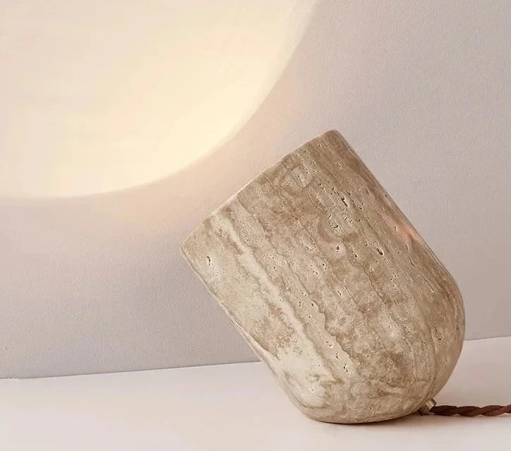 Stone Spotlight Table Lamp in honed travertine finish, sculptural tilted profile directing focused beam upward, artisan craftsmanship with braided cord detail, by Domus Collective.