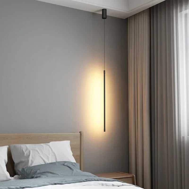Distinctive slim black pendant diffusing soulful warm glow beside neutral linen tones in a calm bedroom sanctuary,theStreamline Shine Suspension Light,by Domus Collective Steel the Show collection.