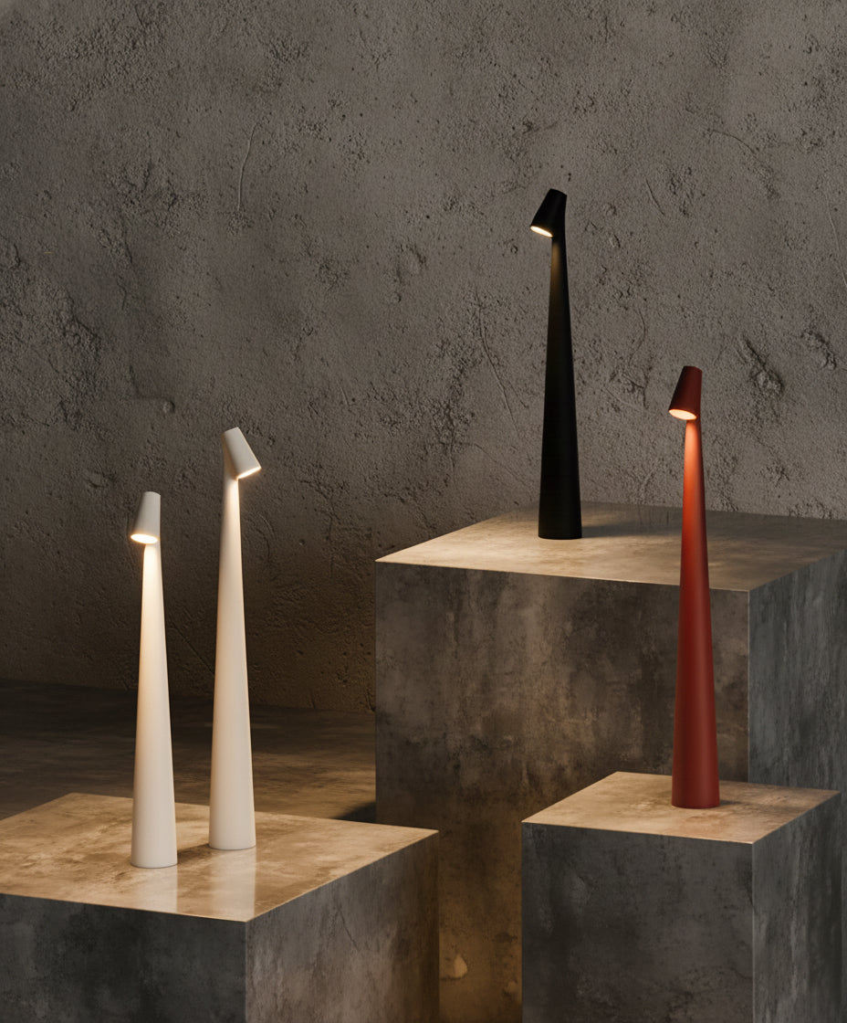 Four Metallic Street Pole Light Portable Lamp by Domus Collective on Sculpturalconcrete platforms with a dark textured wall background. Table lmaps in White, Red and Black.