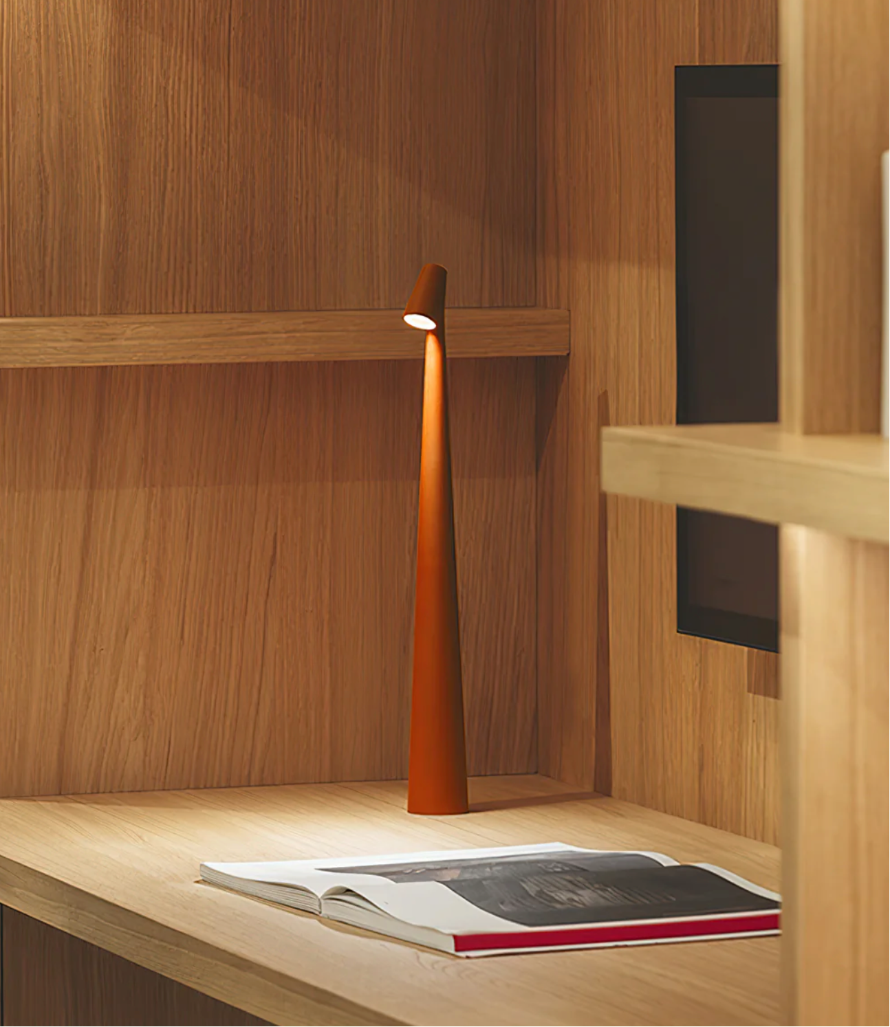 Wooden Oak desk with an orange, metallic Street Pole Light Portable Lamp by Domus Collective and an open book in a room with wooden walls providing light for desk related subjects, like reading,writing or working on a project.