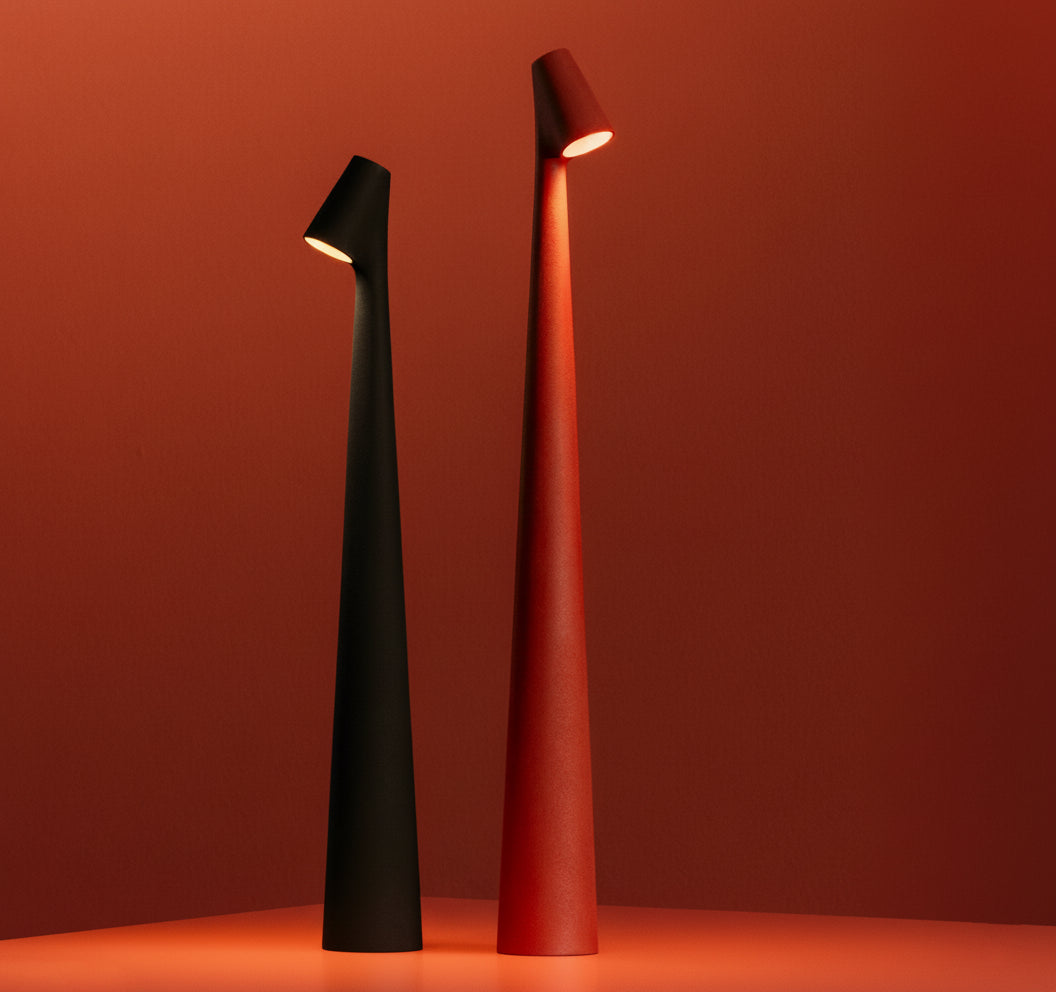 Two Street Pole Light Table Lamps by Domus Collective. All rechargeable, Portable metallic, thin lamps, one black and one red, with timeless design on a matching red background.