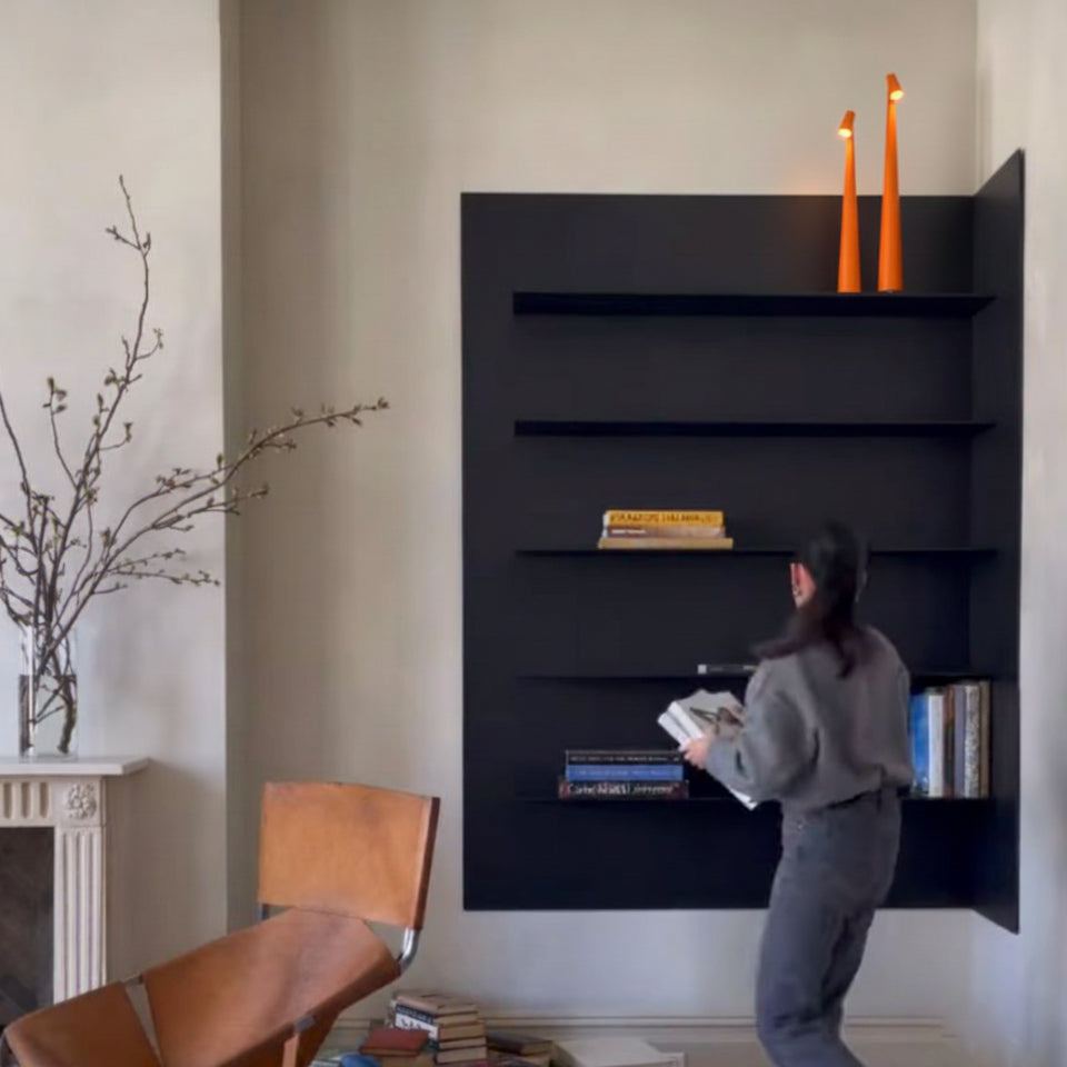 Person interacting with a modern black wall mounted bookshelf in a character filled room featuring Two organge Street Pole Light Portable Lamp by Domus Collective.