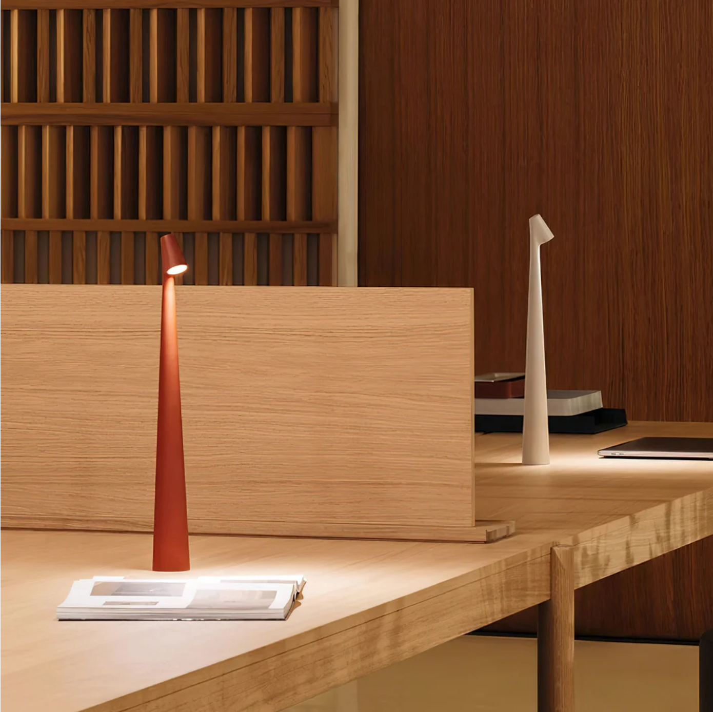 Two Metallic Street Pole Portable Lamp by Domus Collective,one in red and the other in white colour,with elegant tapered cone design,styled on a light wood desk in a warm interior setting made for task lighting