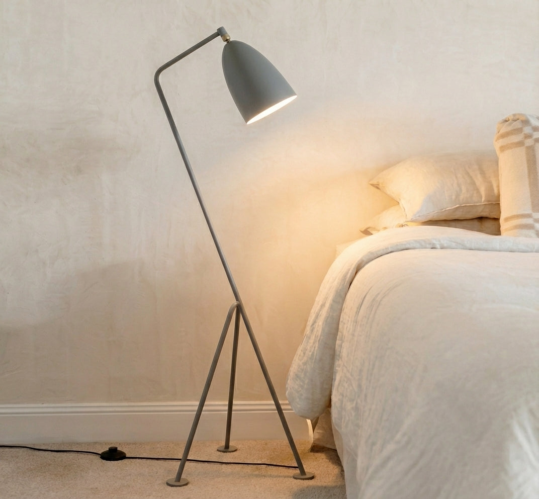 The Long Neck Floor Lamp in grey with minimalist tripod design casting soft illumination beside natural linen bedding by Domus Collective bedside lighting, timeless sculptural form bringing wellbeing-focused warmth.