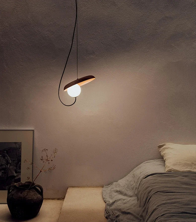 The Orbit Pendant Light by domus collective in rust colour, hanging above a bed in a dimly lit room. This handcrafted planetary pendant adding cosmic elegance to modern spaces, by Domus Collective.