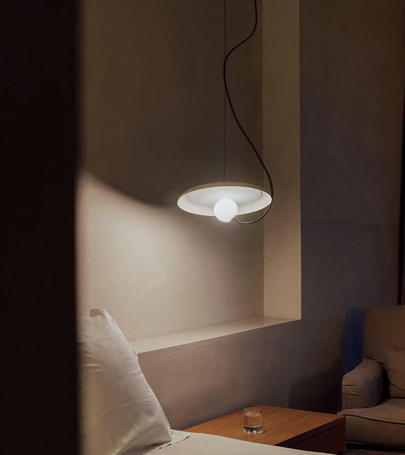 The Orbit Pendant Light D35cm in white colour by domus collective, hanging above a bed with white elegant linen  in a dimly lit room.