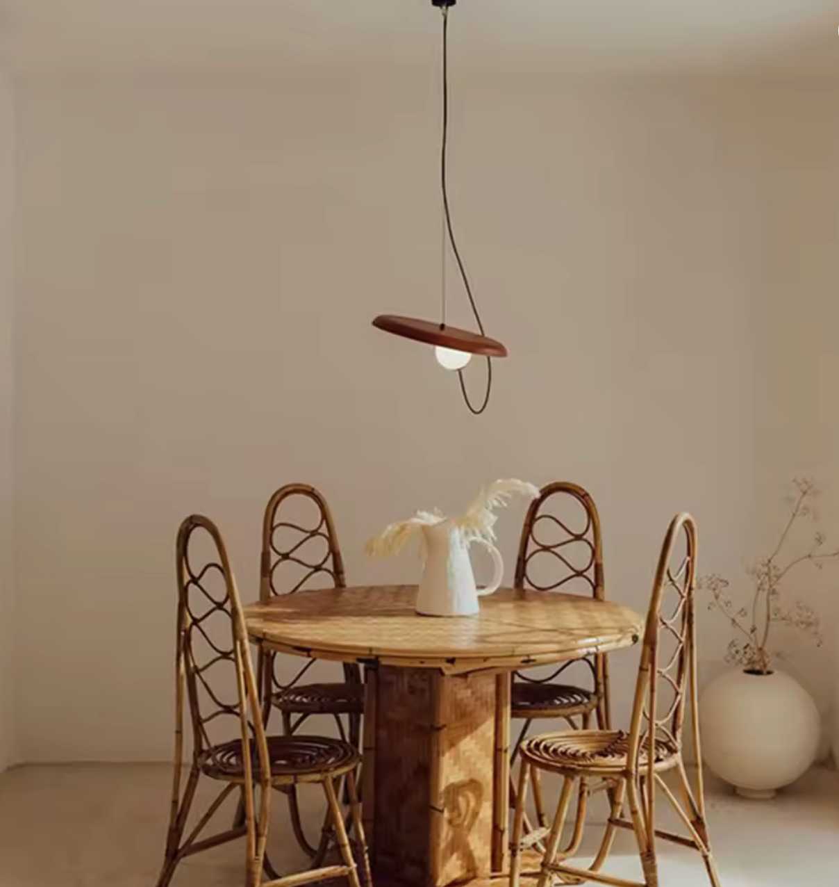 Dining area with bamboo round table and chairs under The Orbit Pendant Light by domus collective in rust colour in a minimalistic space.