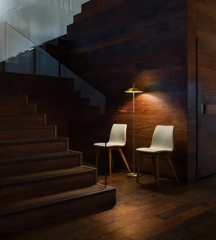 Sculptural brass Toothpick Balance Floor Lamp casting a warm pool of light against rich walnut paneling, understated sophistication for contemporary living spaces, by Domus Collective.
