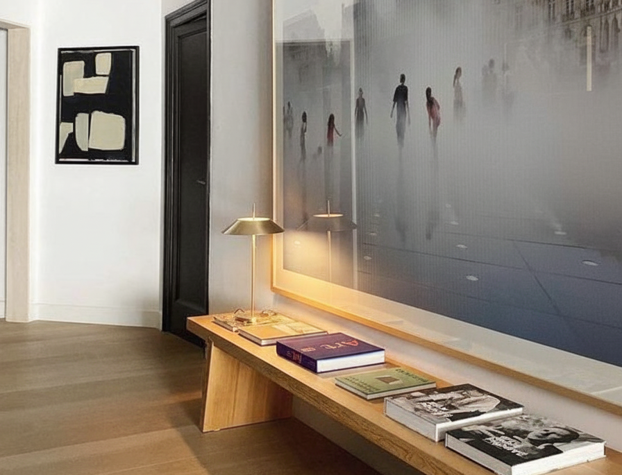 Toothpick Balance Table Lamp in brushed gold finish with wide conical shade and ultra-slim stem on a contemporary wooden bench in a gallery-style hallway, sculptural designer lighting by Domus Collective.