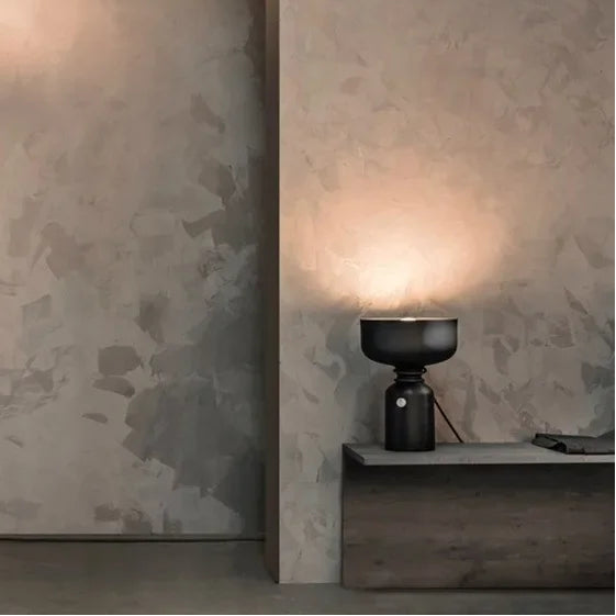 Vessel of Light Floor and Table Lights by Domus Collective,in a minimalist black finish - standing against a textured concrete wall, their sculptural, vessel-inspired forms radiating a warm ambient glow and refined beauty within a calming atmosphere.